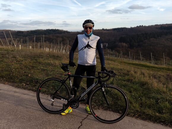 Ich stehe mit meinem Rennrad auf einer Anhöhe in den Weinbergen, im Hintergrund sieht man Reben am Hang